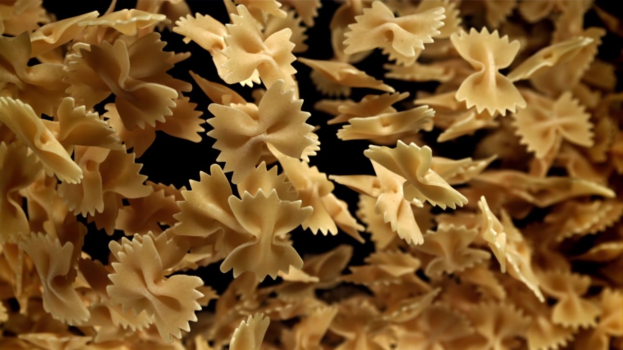 Pasta farfalle secca che cade al rallentatore su sfondo nero.