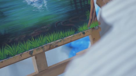 painter brushing grass detail with fine brush on artwork