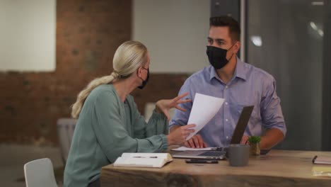 Caucasian-male-and-female-business-colleagues-wearing-masks-in-discussion-at-work