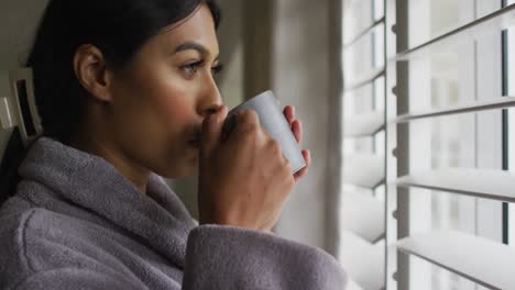 Video-of-biracial-woman-in-rope-with-coffee-looking-outside-window