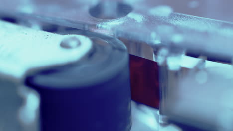 primer plano extremo de la cinta de cinta grabadora de microcassette que se ejecuta bajo el rodillo de presión en luz azul fría