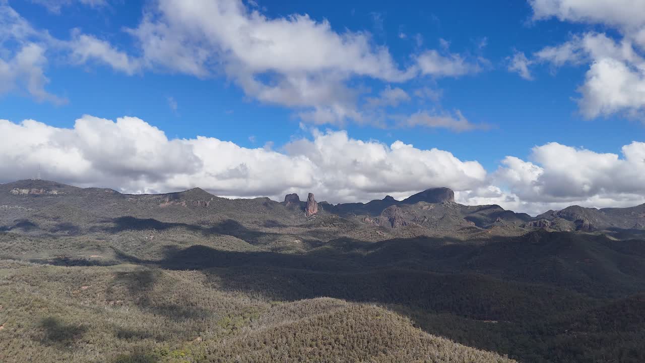 Wide landscape view of Warrumbungle National Park’s volcanic peaks under moving clouds, with shifting sunlight and dynamic shadows, captured in daylight with a steady camera