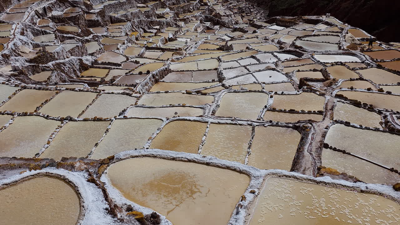A stunning cinematic tilt shot reveals the impressive terraced salt pools of the Maras Salt Flats, showcasing this unique and beautiful landscape in the Sacred Valley, Peru