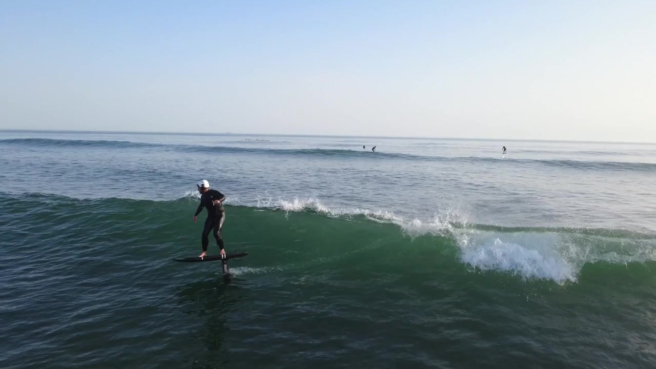 Un rider di surf foil che lascia un'onda con velocità per connettersi alla successiva durante un tramonto mozzafiato in Portogallo, combinando fluidità, controllo e prestazioni oceaniche