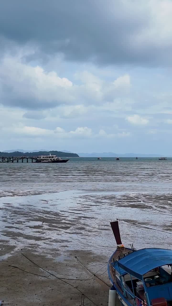 Aerial view of boats stranded at low tide near a pier in Phuket, Thailand, under cloudy skies, capturing serene coastal life