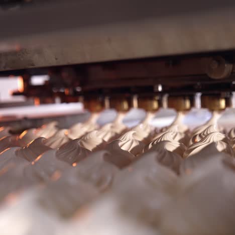 a number of freshly-made creamy marshmallows moving on the conveyor line. new marshmallows being squeezed at the backdrop. close view
