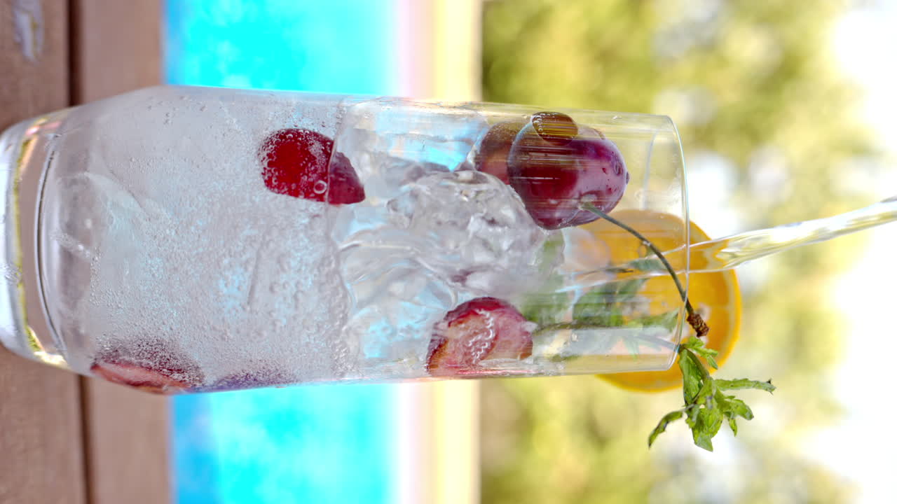 Mojito cocktail glass with ice and cherry and mint, soda and gin near a blue pool close up