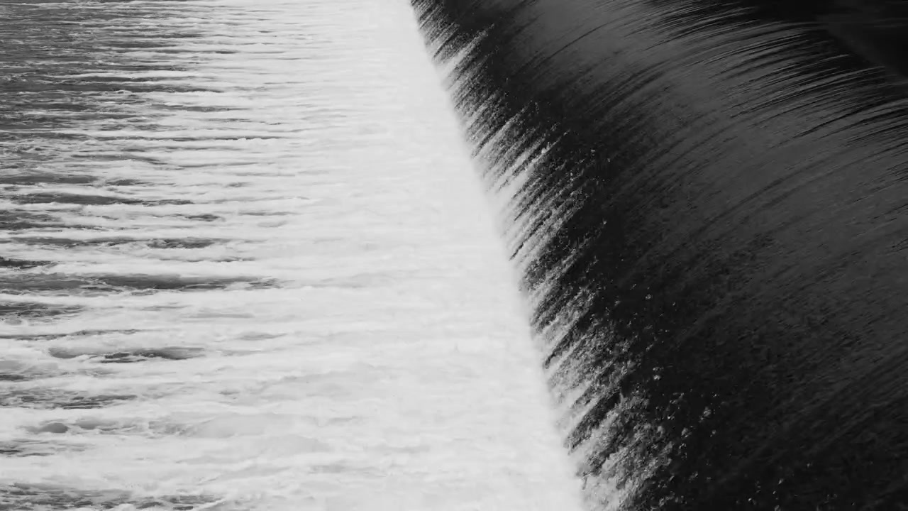 ダムを滑らかに流れる水のモノクロの景色。印象的な線と質感のある模様を作り出す。日中のイギリス、スコットランドの平和な淡水の風景。