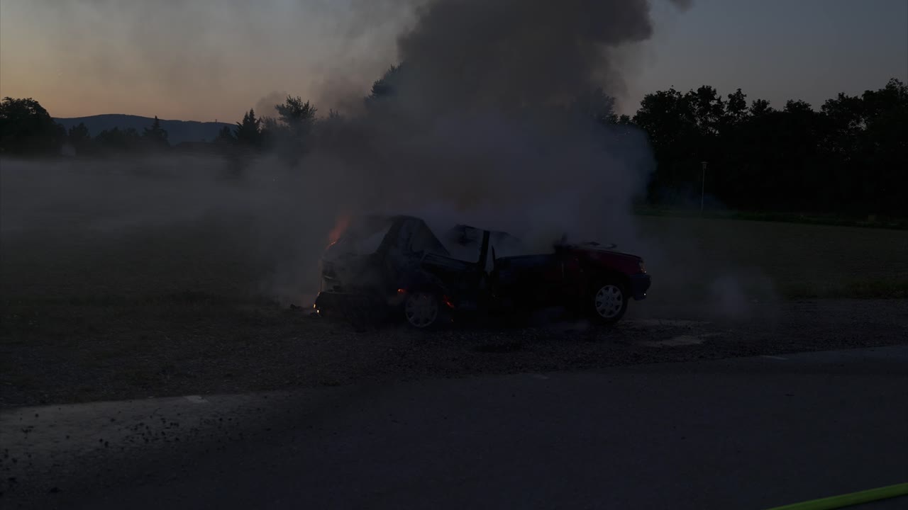 Burning car in the evening hours is extinguished with water from the left - the fire is already almost gone - Slow Motion