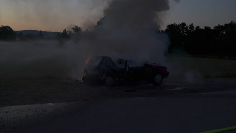 burning car in the evening hours is extinguished with water from the left - the fire is already almost gone - slow motion