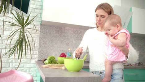 mother holding baby on hands in kitchen. mom with kid prepare dinner