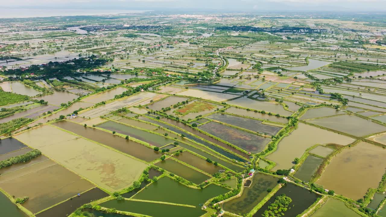 Drone tilts up above coastal fishponds in Lingayen Pangasinan sunny cloudy day