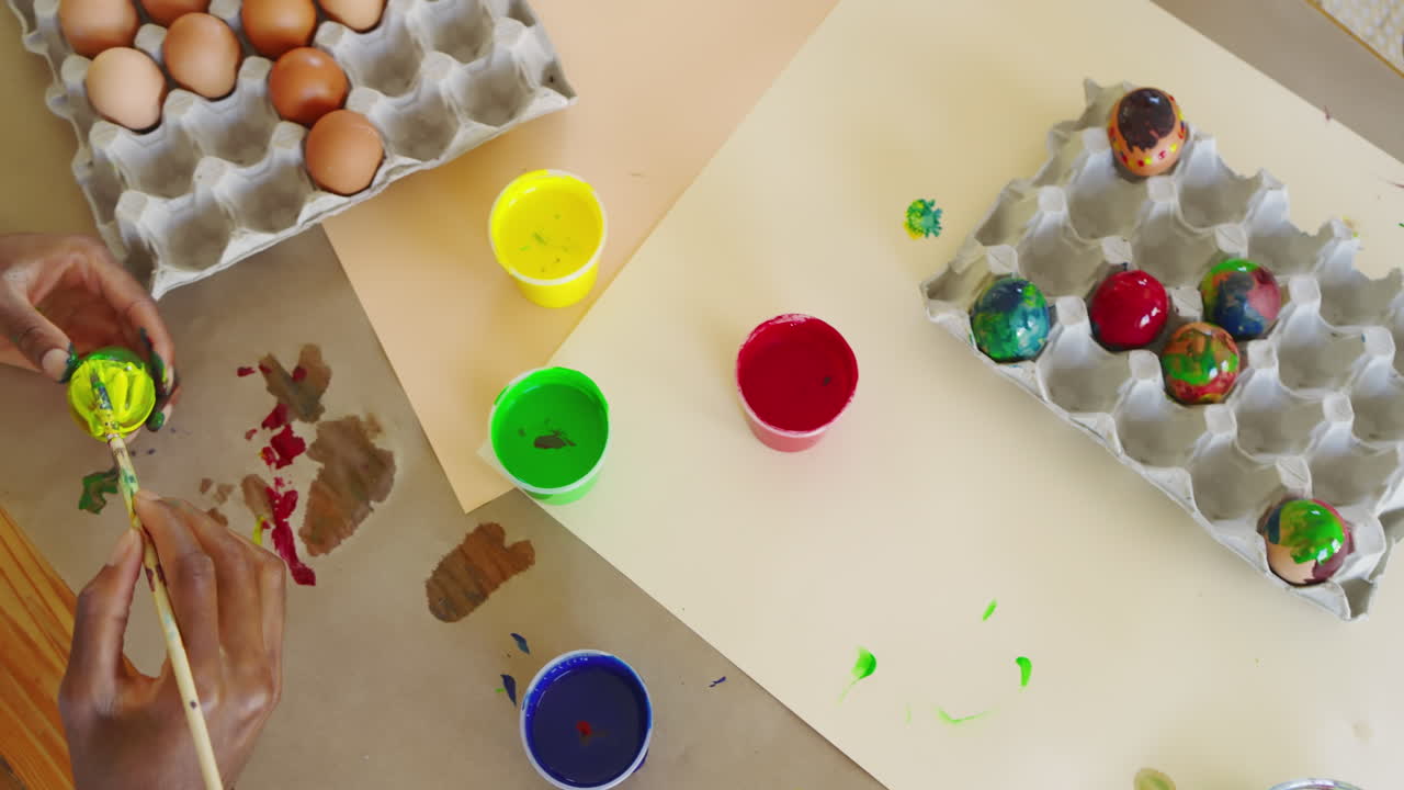 Easter, diverse family painting eggs with colorful paints at home, sharing creative activity