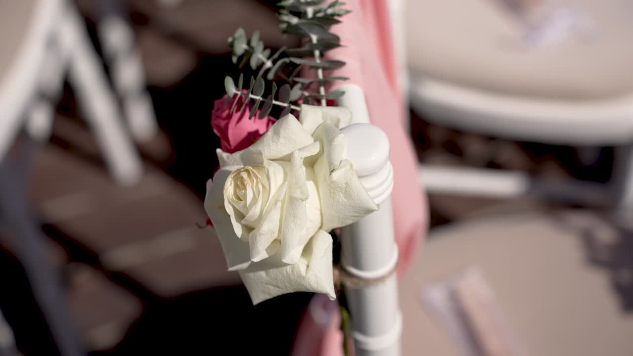Flowers are arranged on chairs for a gathering in a garden. Guests are expected to arrive soon. The setting is bright and the decorations are simple and elegant