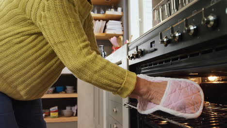 old lady wearing oven gloves taking out freshly baked muffins from oven 4k 4k