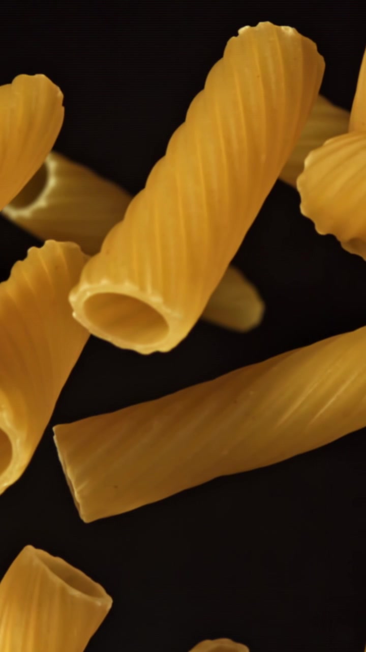 Rigatoni secchi che cadono al rallentatore su sfondo nero