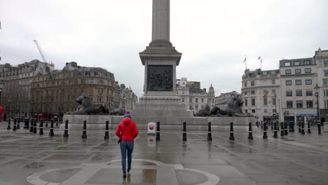 Young-woman-tourist-walking-towards-Nelson's-column-in-an-empty-Trafalgar-Square,-London