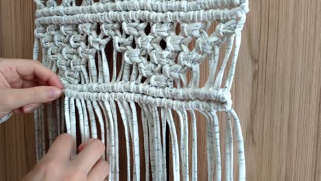 close up of females hands doing knots making a macrame decoration with white and grey cloth stripes