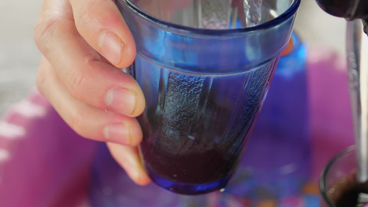 Ripresa al rallentatore, acqua versata in una tazza di caffè Lombok, portabicchieri rosa sullo sfondo