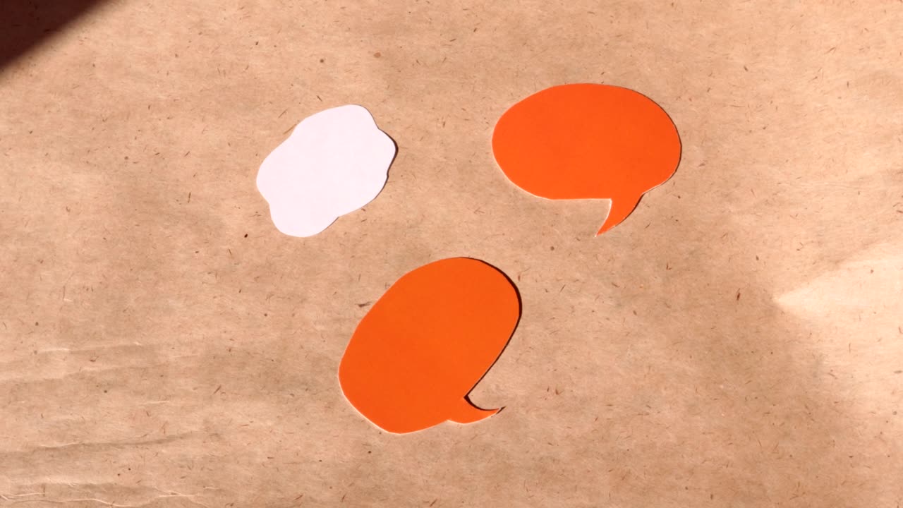 Video 4K, primo piano di due fumetti ritagliati da carta arancione e una nuvola bianca, con spazio per il testo. Concetto fai da te. Ruota su carta kraft marrone, vista dall'alto.