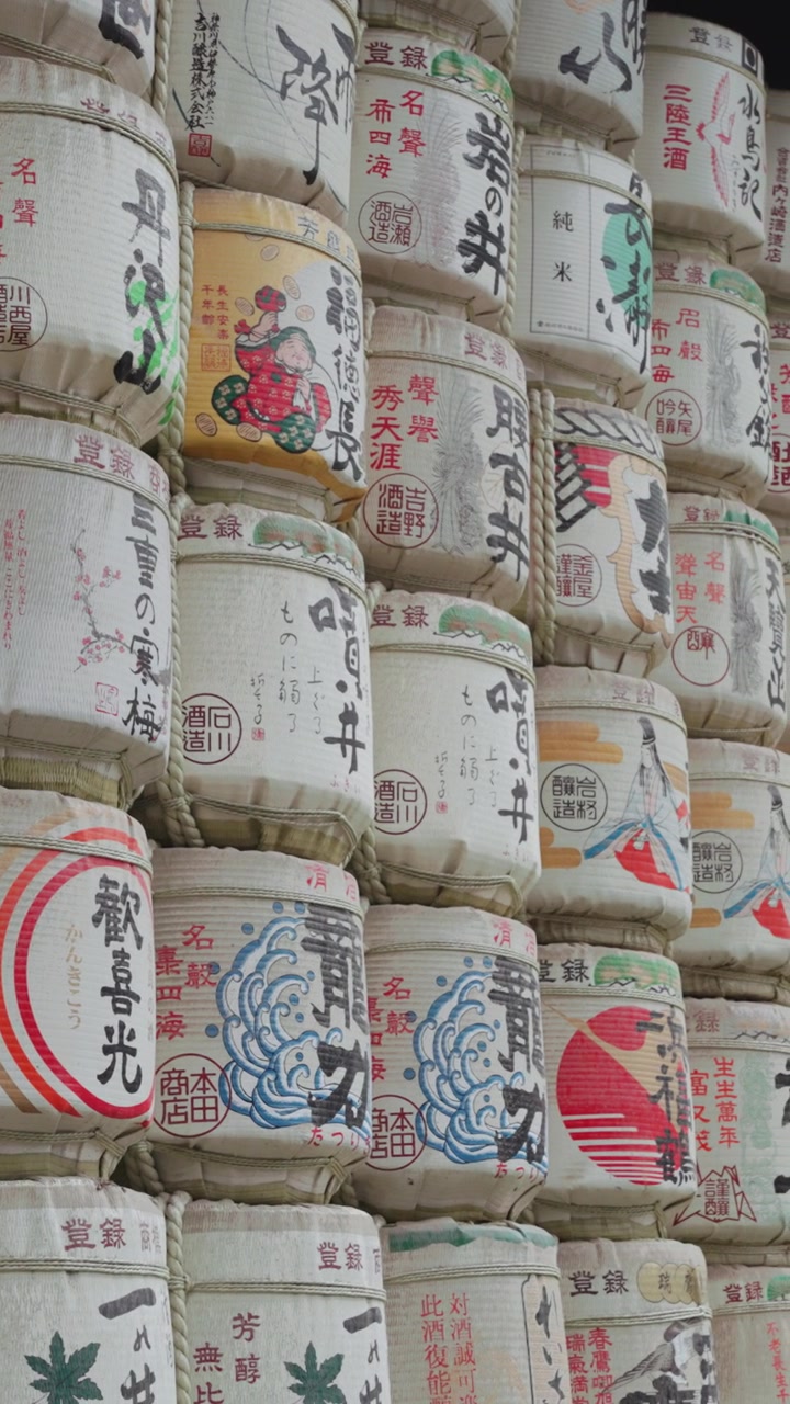 Vertical slow panning video of beautifully decorated sake barrels at Meiji Jingu Shrine during the daytime in Yoyogi Park in Tokyo.