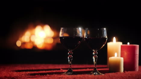 glasses of wine and candles on a table with a red tablecloth in the background a fireplace