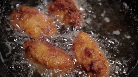 four crispy spanish croquetas deep fry in bubbling oil, close up