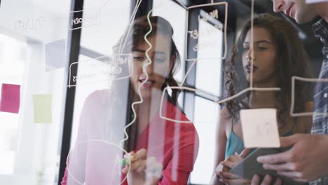 Diverse-creative-colleagues-in-discussion-making-notes-on-glass-wall-in-office,-slow-motion