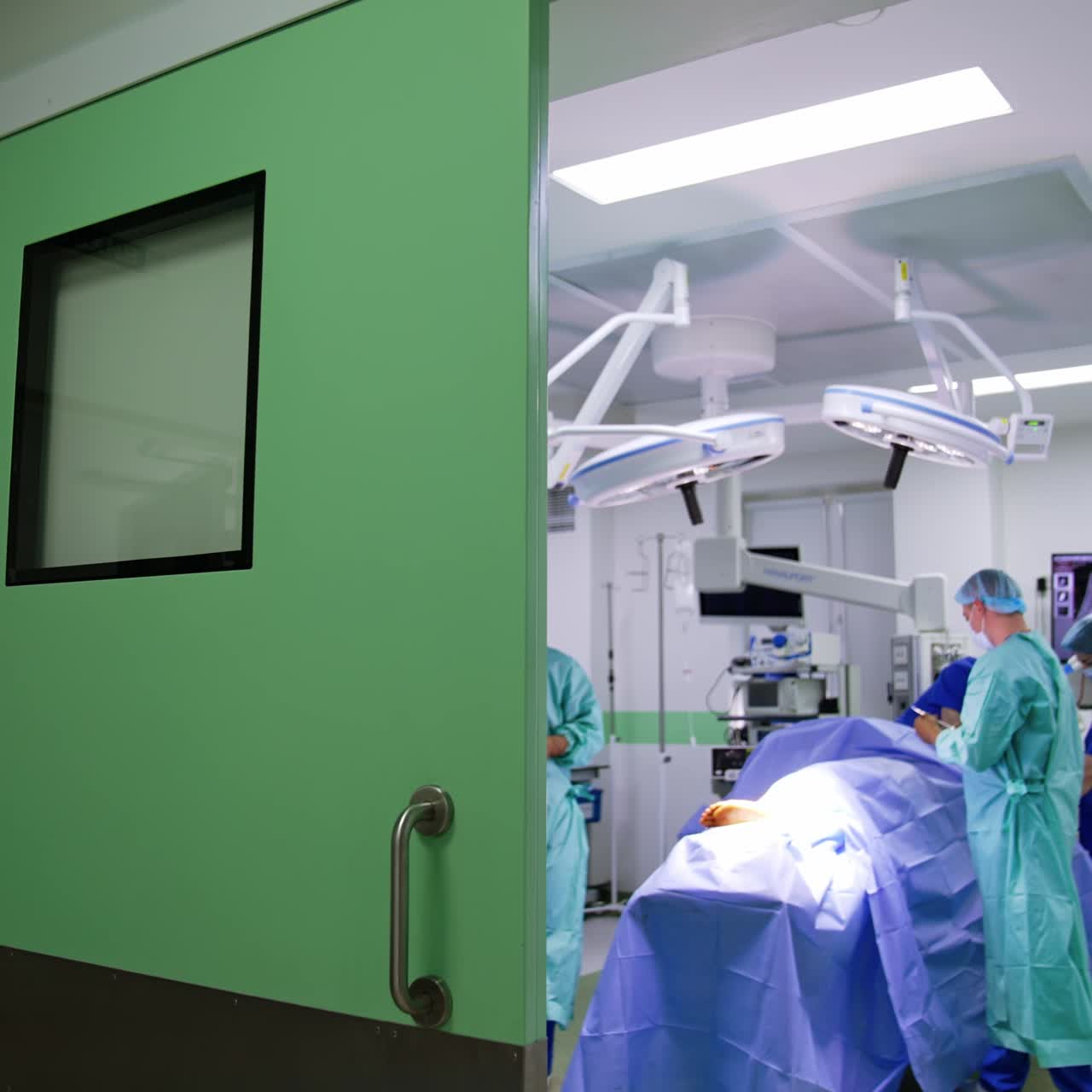 De pie en la puerta abierta de una sala de cirugía. El personal médico prepara al paciente para la operación.