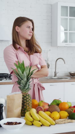 young woman in the kitchen. fresh fruit and vegetables on the table for dieting. expressive female trying to prepare healthy food at home. vertical video