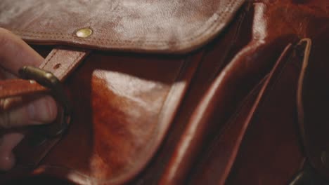 a person closing the strap on the front part of a brown leather bag