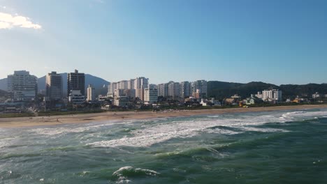 drone shot of praia brava in brazil with the sea and buildings on the background