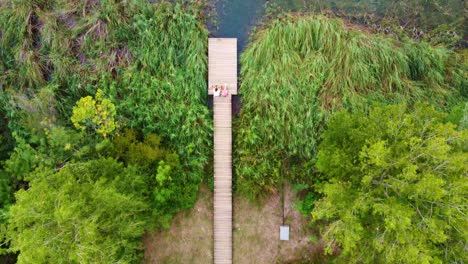 volando sobre una pareja sentada en una plataforma de madera frente a un lago con agua clara, entre los árboles, en banyoles, cataluña, españa