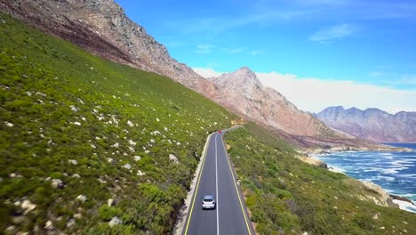 Coche-Conduciendo-Por-La-Soleada-Carretera-De-Montaña---Costa,-Ruta-Jardín-Sudáfrica,-Seguimiento-Aéreo-Hacia-Adelante