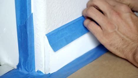 4k, painter using masking blue tape to secure baseboard, moulding. preparation for room painting.