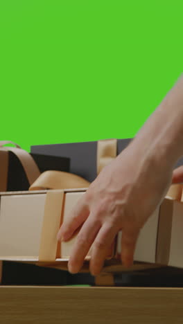 video vertical de un hombre recogiendo regalos en cajas envueltas en regalos decoradas con cinta en la mesa disparado contra una pantalla verde