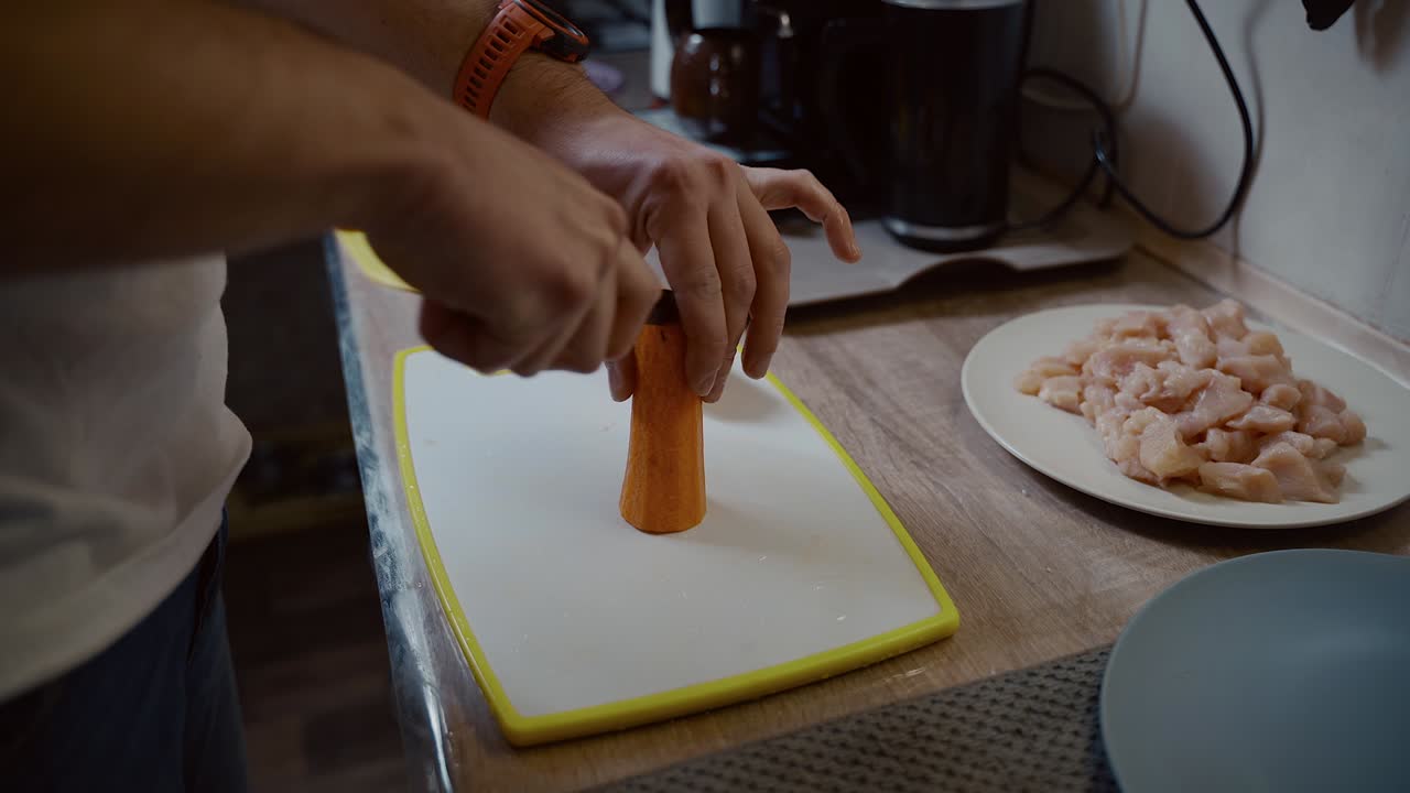hombre cortando rebanada de zanahoria en la cocina en casa. comida de dieta saludable. hombre joven cortando zanahorias en la tabla de cortar. chico prepara comida en la cocina. él cortando zanaha en casa. practica la cocina.