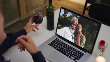 Mid-section-of-african-american-woman-drinking-wine-while-having-a-video-call-on-laptop-at-home