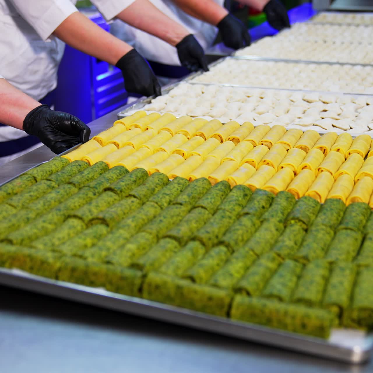 Cooks in white outfit put the metal trays with prepared food on the table. Beautifully laid crepes and ravioli at restaurant
