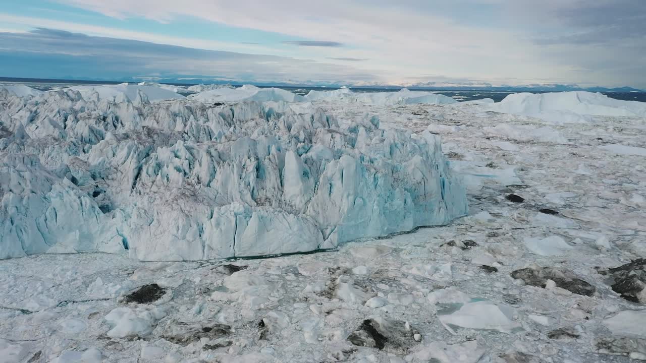 Aerial drone view of a towering glacier wall surrounded by a frozen landscape in Greenland, showcasing the dramatic beauty and scale of the Arctic environment