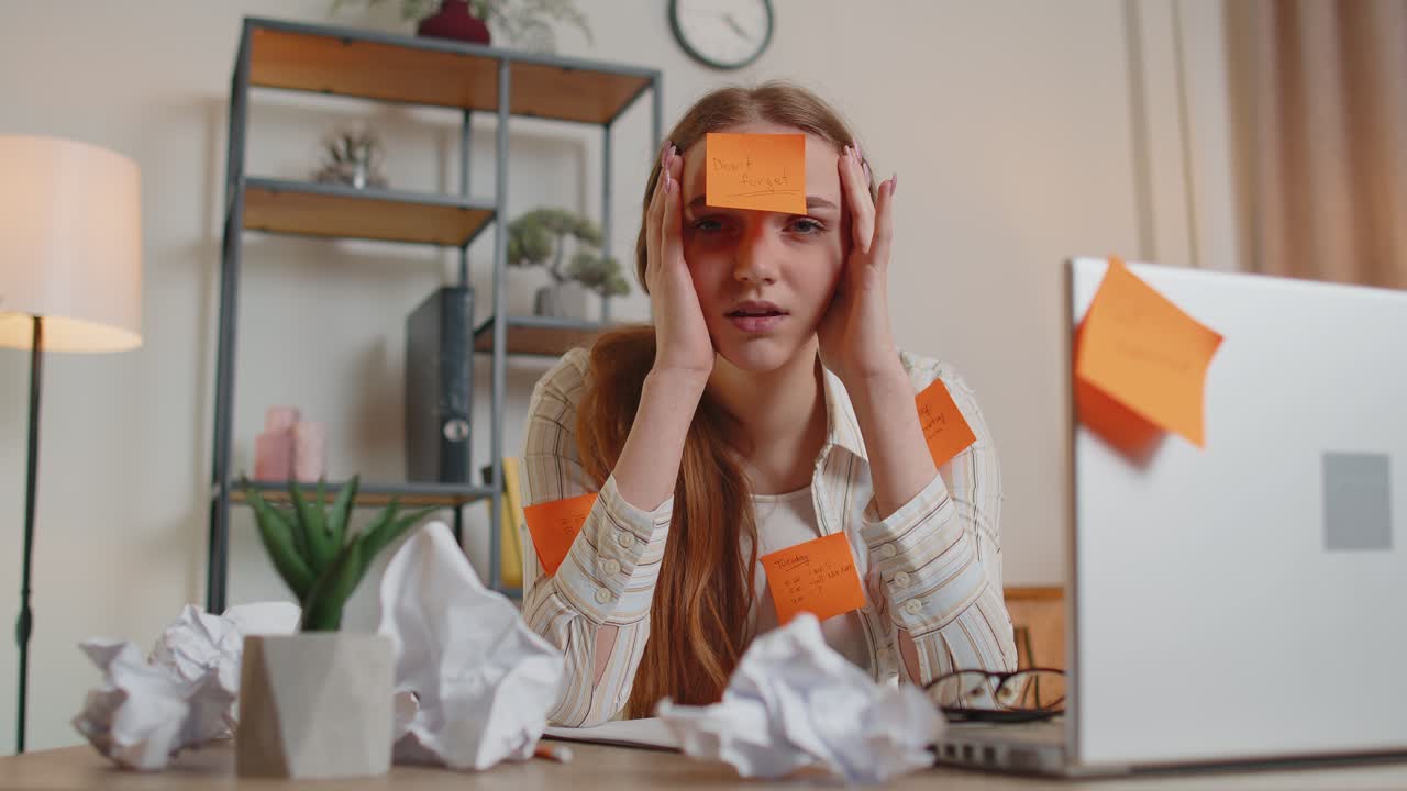 измотанная женщина-фрилансер с наклеенными наклейками, использующая ноутбук, имеющая проблемы с концентрацией в офисе