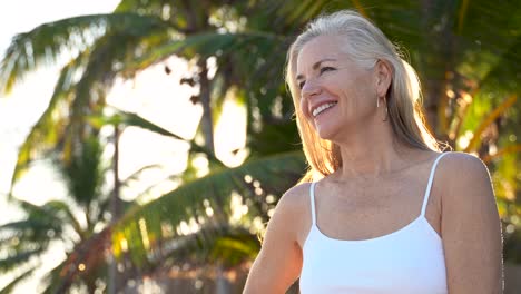 With-one-arm-up-holding-her-blonde-and-gray-hair-a-mature-woman-looks-and-smiles-at-the-camera-and-then-looks-to-the-left