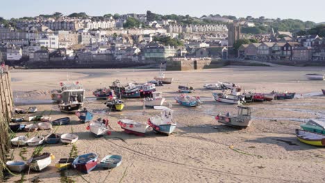 fishing boats moored on the harbor during lowtide with st ives town in the background in cornwall, england, united kingdom