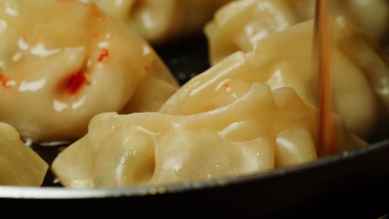 Drizzling Chili Sauce Over Pan-Fried Dumplings in a Pan