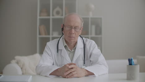 un anciano médico está sentado en la clínica y escuchando durante una videoconferencia en línea asintiendo con la cabeza