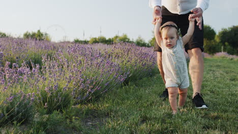 dad teaches his daughter to walk, the child takes the first steps, holding hands of his father. baby's first successes.