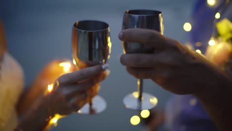 bride and groom clinking silver glasses surrounded by lights at night