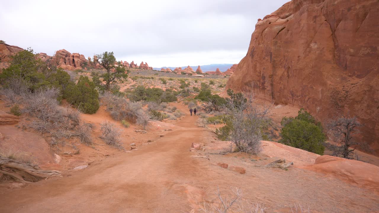 Ripresa inclinata di persone che fanno escursioni nel Parco Nazionale di Arches verso l'Arco del Paesaggio in una giornata nuvolosa.