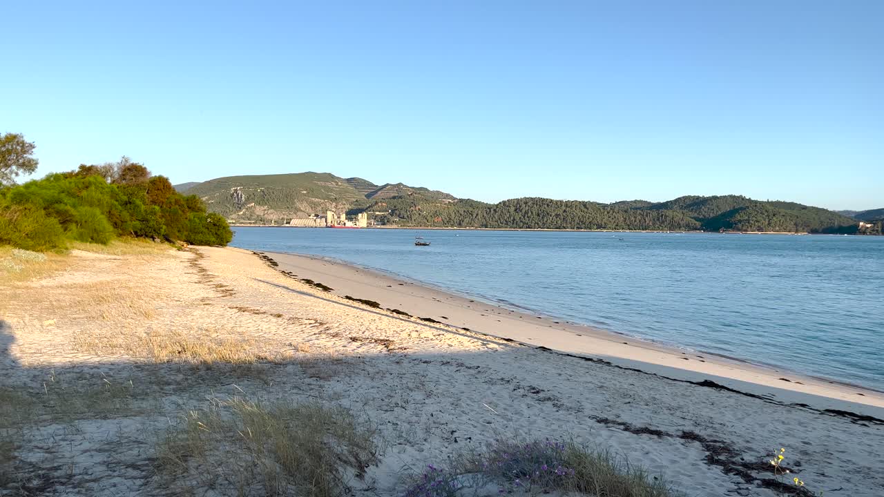 Close-up view of the beach with small waves reaching the shore, with the Arrabida mountains in the background during sunrise