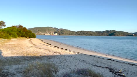 Nahaufnahme-Des-Strandes-Mit-Kleinen-Wellen,-Die-Das-Ufer-Erreichen,-Mit-Den-Arrabida-Bergen-Im-Hintergrund-Bei-Sonnenaufgang